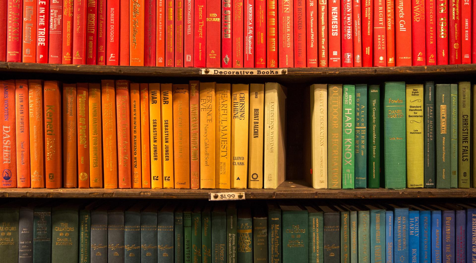 Three shelves of books organized by their cover colors